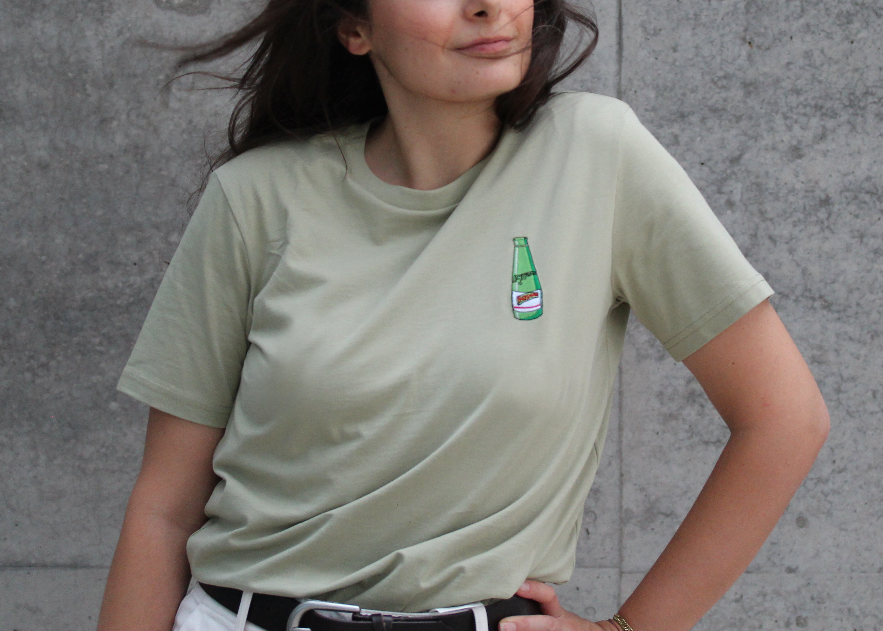 Frau trägt nachhaltiges T-Shirt in sage Green mit einer gestickten Beypazari gazoz Flasche auf der Brust.