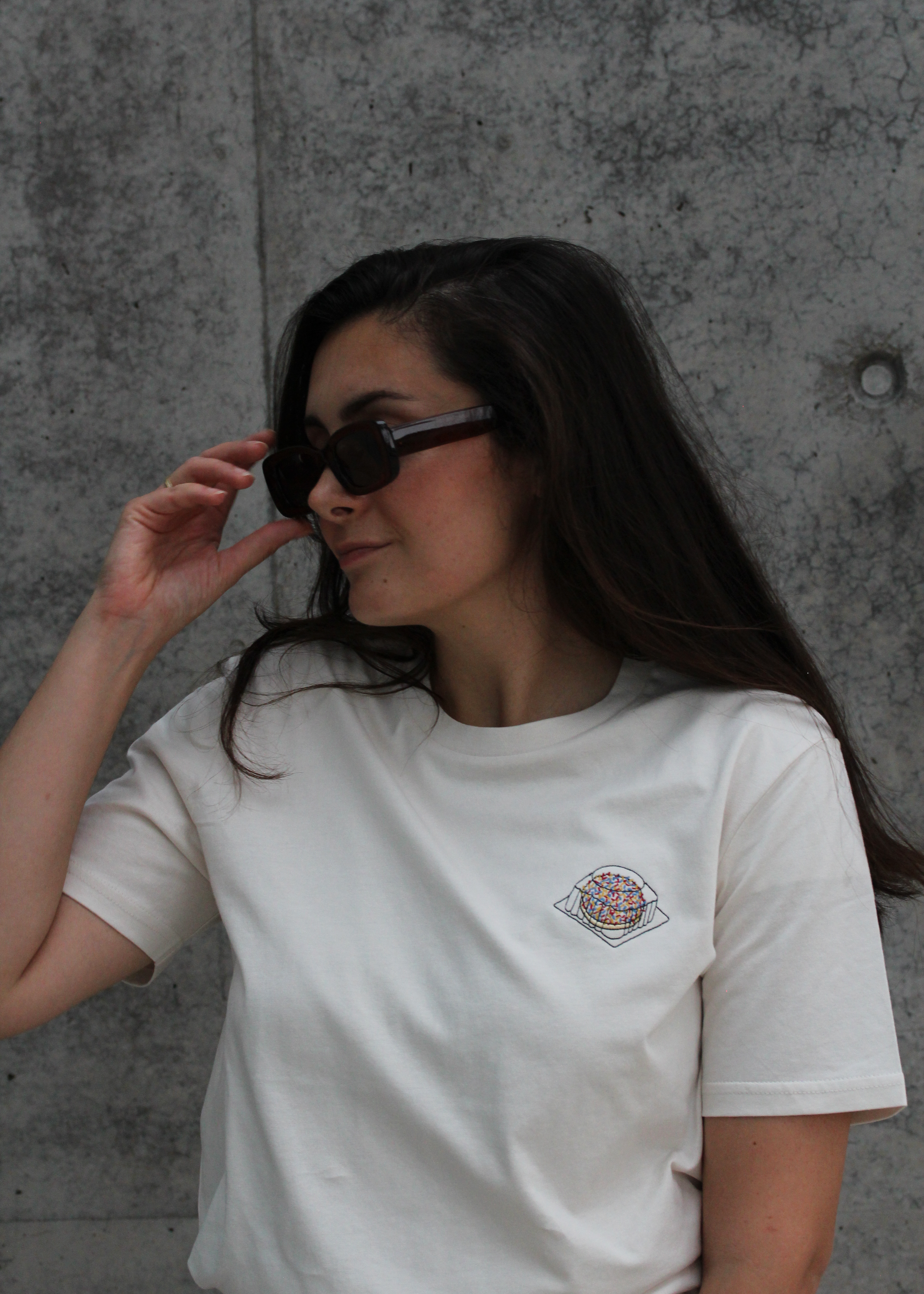 Frau mit Sonnenbrille trägt nachhaltiges T-Shirt aus Bio-Baumwolle in Vintage white. Auf der Brust ist ein Eti-Puf Törtchen gestickt. 